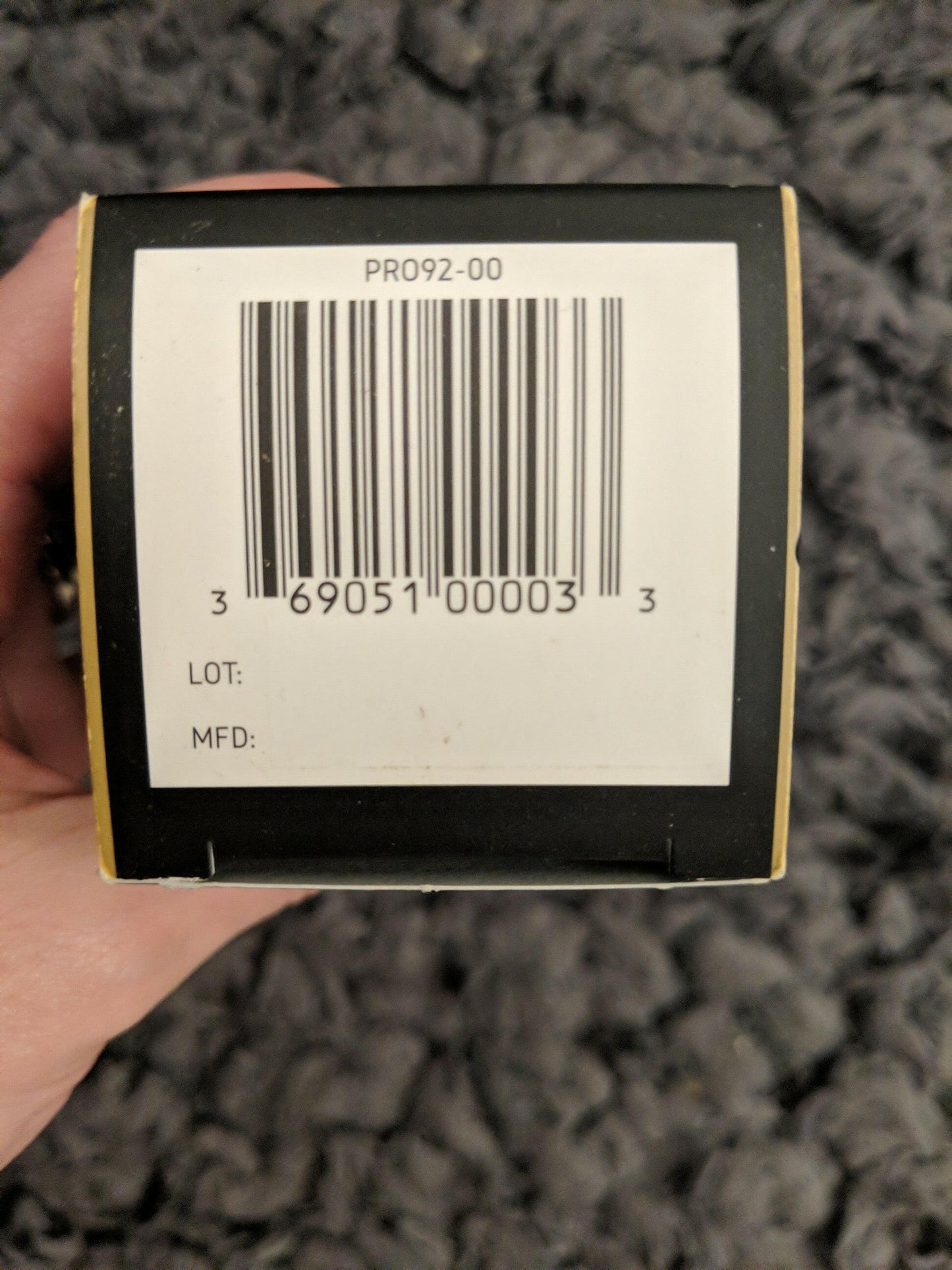 Bar code label on a product packaging held by a hand against a textured gray background