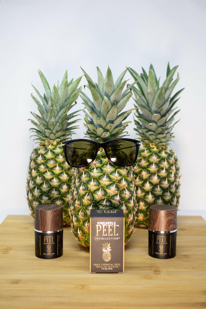 Three pineapples with sunglasses and two bottles on a wooden surface